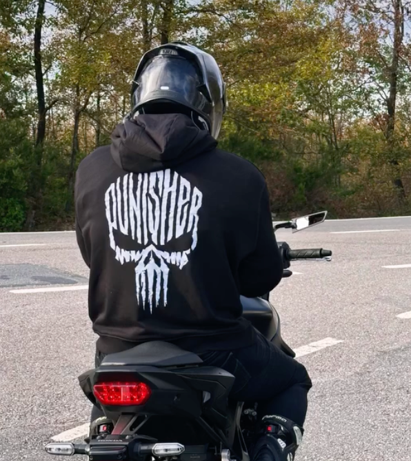 Kasklı sürücünün sırtında Punisher reflektörlü siyah hoodie, motosiklet üzerinde arkadan görünüm