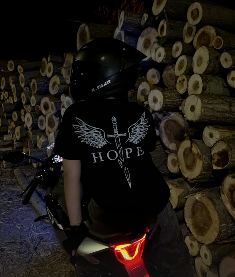 Gece motosikletin yanında Hope reflektör baskılı siyah tişört giyen sürücü