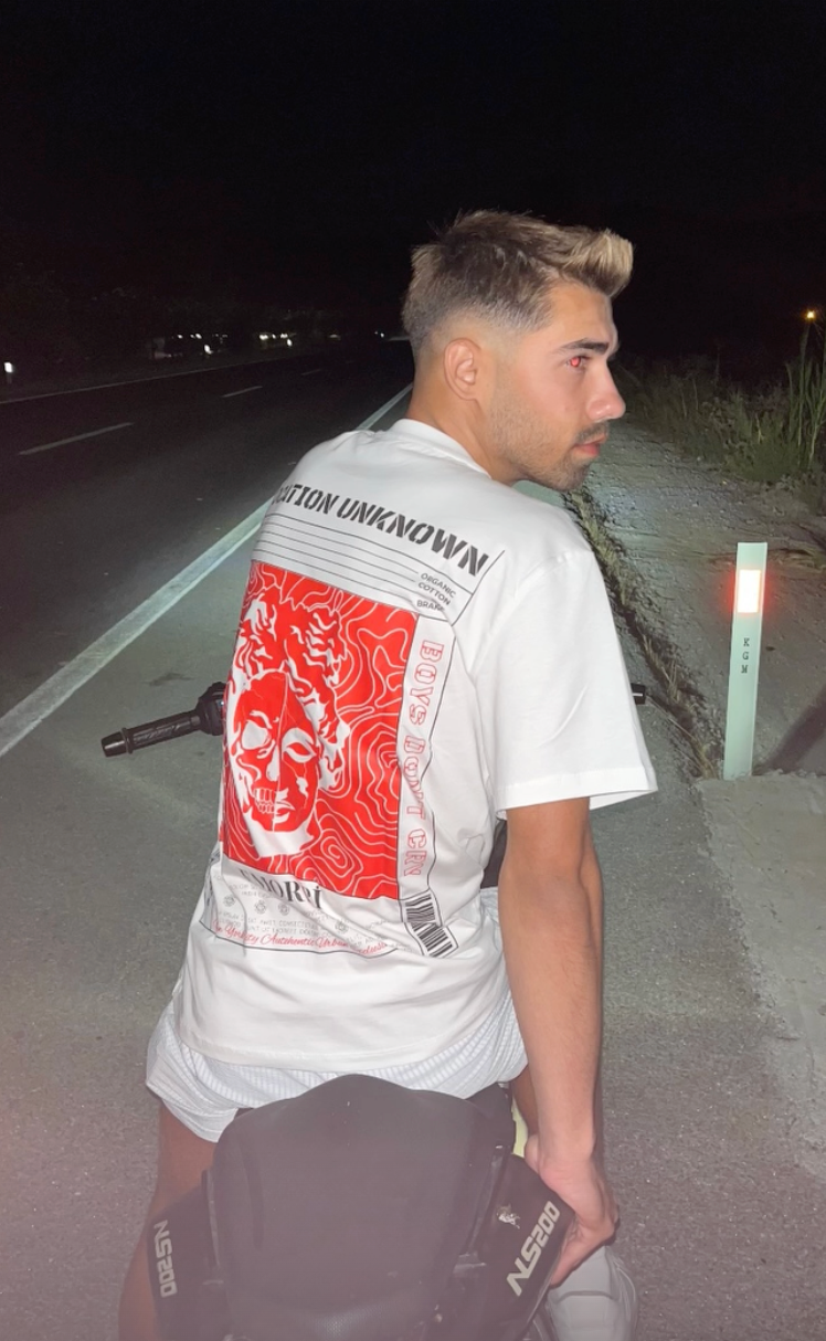 Gece yolda Location Unknown baskılı beyaz motorcu tişört giyen kişi, arkadan görünüm
