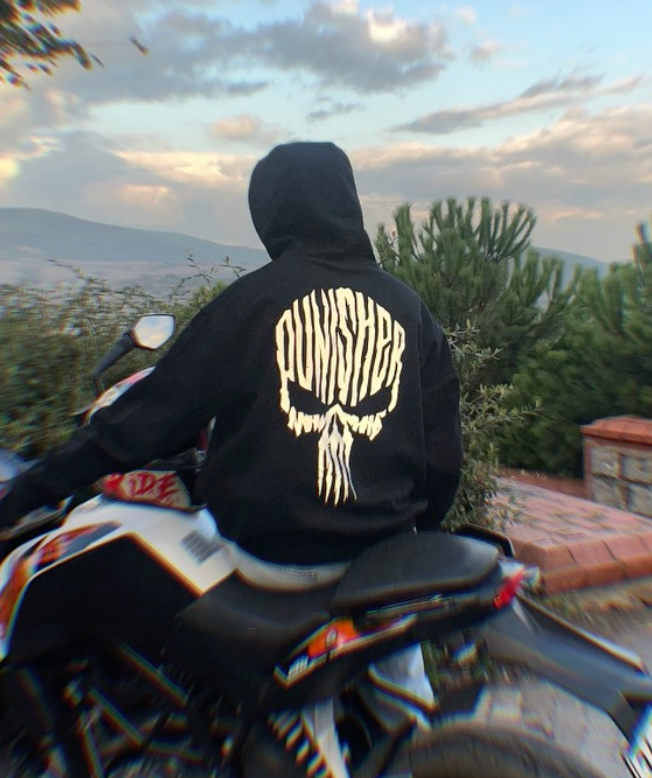 Motosiklet üzerinde Punisher reflektörlü hoodie giyen sürücü, sırtta parlayan kurukafa baskısı