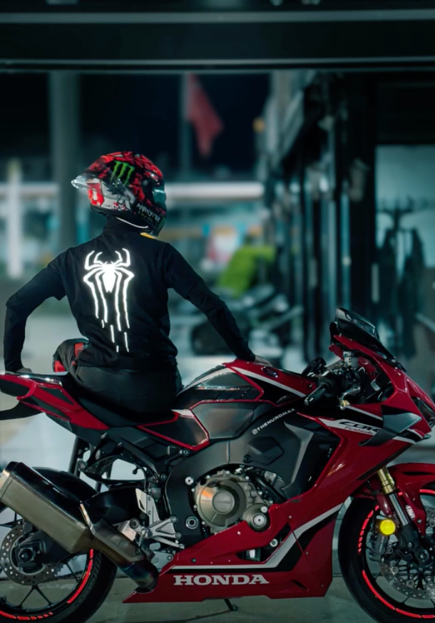Kırmızı motosiklet üzerinde Spider reflektör baskılı siyah tişört giyen kasklı sürücü