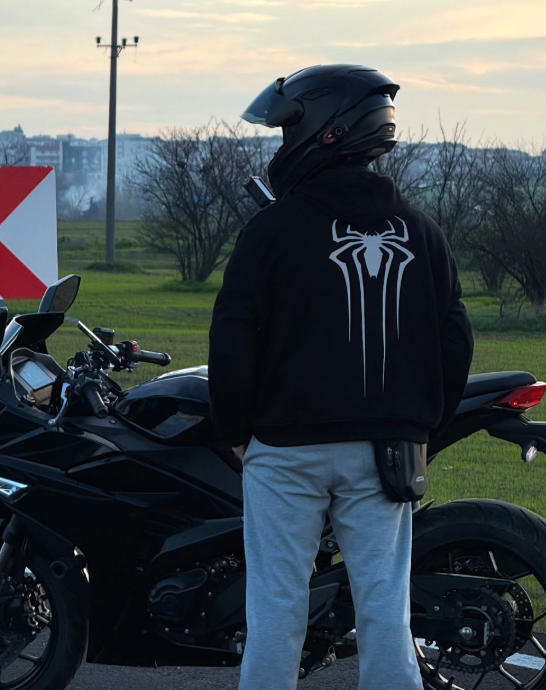 Kasklı sürücü motosikletin yanında Spider reflektörlü siyah hoodie ile, arkadan görünüm