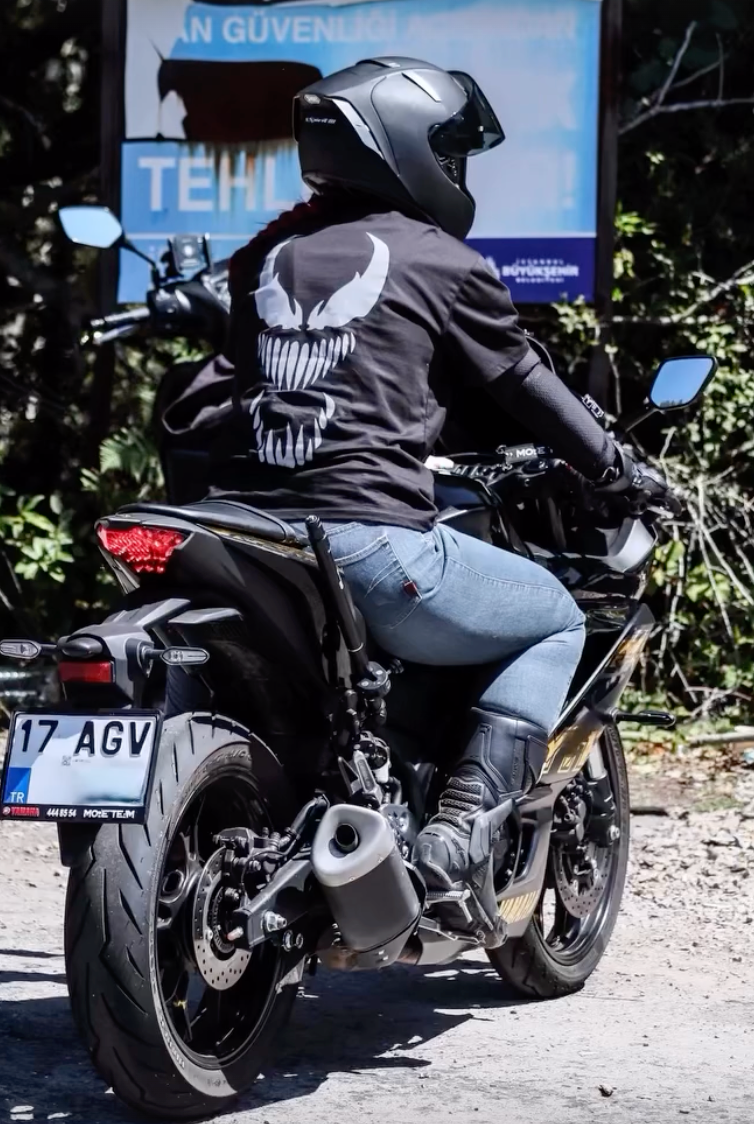 Motosiklet üzerinde Venom reflektör baskılı siyah tişört giyen kasklı sürücü